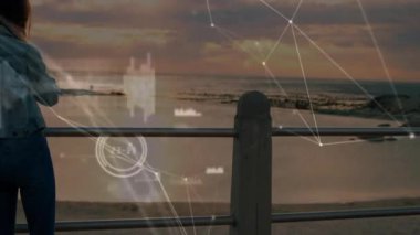 Gün batımında okyanusun kenarında durmuş, ağ bağlantıları ile canlı yayın yapan bir kadın. Teknoloji, dijital, ağ, yenilik, fütüristik, iletişim