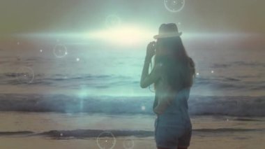 Şapkalı bir kadın dijital ağ animasyonu ile okyanus dalgalarını fotoğraflıyor. Fotoğraf, plaj, teknoloji, bağlantı, açık hava, tatil