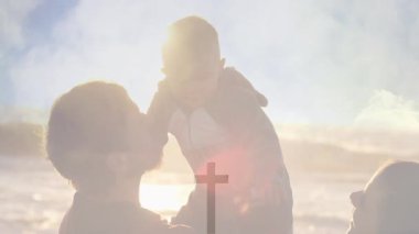 Siluetli ve çocuklu bir ailenin canlandırması ve parlak gökyüzüne karşı haç sembolü. Birlik, inanç, umut, maneviyat, birliktelik.