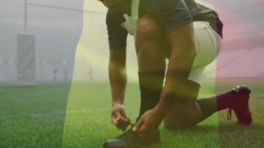 Sahada, rugby oyuncusu ayakkabı bağcıklarını bayrak renklerinin animasyonuyla bağlıyor. Sporcu, hazırlık, spor giyim, yarışma, takım ruhu, ulusal gurur