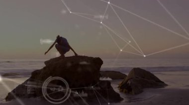 Okyanus kenarındaki kaya üzerinde oturan kişi ağ bağlantıları ile animasyon örtüşüyor. Teknoloji, bağlantı, iletişim, dijital, geleceksel, ağ