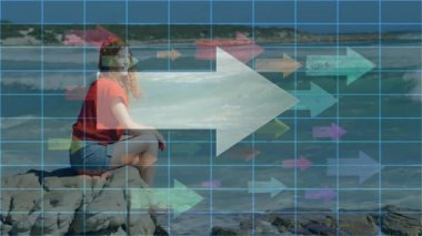 Dijital şebeke animasyonu ile okyanus kenarındaki kayalarda oturan kadın. Teknoloji, fütüristik, doğa, yenilik, artırılmış manzara