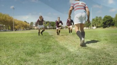 Açık mavi gökyüzünün altında çimenlik alanda rugby oynuyorlar, sporcular iş başında. Takım çalışması, sportmenlik, rekabet, atletizm, açık hava, spor