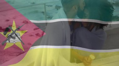 Sahilde kucaklaşan Mozambik bayrak animasyonu arka planda olan çift. Romantizm, kutlama, seyahat, vatanseverlik, okyanus, günbatımı