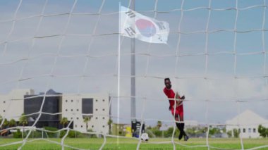 Animasyonda, kırmızı üniformalı futbolcu Güney Kore bayrağıyla kale direğinin yanında. Spor, atlet, aksiyon, rekabet, takım, kutlama