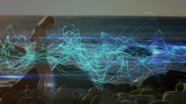 Kayalık sahilde mavi ışık yollarıyla yürüyen bir kadın okyanus üzerinde animasyon yapıyor. dijital, gelecekçi, doğa, eğlence, manzara, yaratıcılık