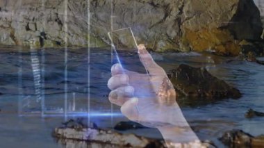 Akıllı telefonu kayalık kıyı şeridinde tutmak, dijital veri animasyonunu ekranda göstermek. Teknoloji, yenilik, mobil, okyanus, arayüz, kıyı şeridi