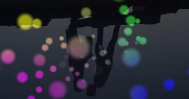 Gün batımında suyun kenarında duran çift siluetinin üzerinde renkli bir bokeh animasyonu. Romantik, sakin, sakin, canlı, akşam, rüya gibi.