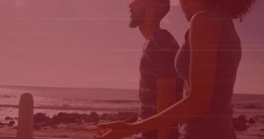 Kumsalda yürüyoruz, pembe gökyüzünün altında, arkalarında okyanus dalgaları olan bir çift. Romantik, günbatımı, sahil, tatil, aşk, sükunet