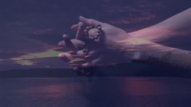 Gün batımı animasyonu sırasında huzurlu gölü yansıtan dua boncukları ve eller tutuyordu. Meditasyon, maneviyat, sükunet, alacakaranlık, yansıma, huzur