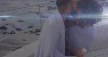 Battaniyeye sarılmış, ışıl ışıl ışık animasyon efektleriyle okyanusu izleyen bir çift. Romantik, gevşeme, sakinlik, alacakaranlık, huzur