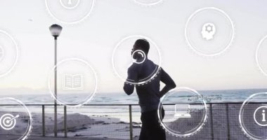 Okyanus kenarında koşan adam, manzarada dijital animasyon simgeleriyle etkileşime giriyor. Fitness, teknoloji, egzersiz, sanal, fütürist, açık hava