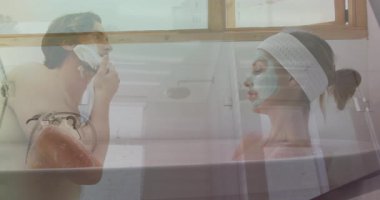 Banyoda, kadın maskeyle dinlenirken erkek tıraş oluyor, animasyondan zevk alıyor. Tımar, cilt bakımı, rahatlama, sağlık, güzellik, çift