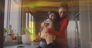 Mutfakta gülümseyen ve sarılan iki kadın, günbatımı animasyonlarıyla örtüşüyor. Arkadaşlık, mutluluk, ev, birliktelik, sıcaklık, bağ.