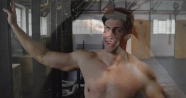 Spor salonundaki adam özgüvenle gülümsüyor, egzersiz ekipmanları ve animasyonlarla çevrili. Fitness, egzersiz, eğitim, kararlılık, motivasyon, güç