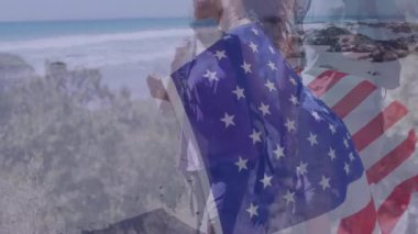 Sahilde yürürken, arka planda Amerikan bayrağı animasyonu ve okyanusu olan insanlar. Vatanseverlik, kıyı şeridi, kum, kutlama, ulusal, birlik