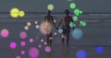 Sahilde yürüyen, renkli bokeh animasyonlarıyla çevrili bir çift. Romantizm, tatil, okyanus, günbatımı, rahatlama, aşk