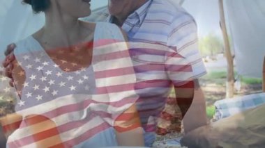 Amerikan bayrağı animasyonuyla kucaklaşan çift açık havada, birlikte gülümsüyor. Vatanseverlik, mutluluk, ilişki, aşk, kutlama, birlik