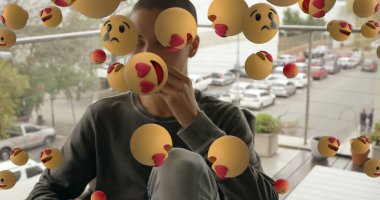 Balkonda oturan genç adam havada süzülen simgelerle çevrili, hayatı düşünüyor. Düşünce, yalnızlık, düşünceler, dijital, emojiler, yansıma