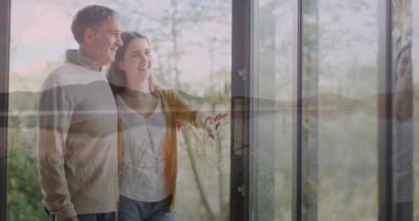 Geniş pencerenin önünde durup doğanın manzaralı animasyonunu izleyen bir çift. Rahatlama, rahatlama, manzara, dinginlik, teknoloji, panoramik