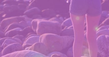 Kayalık sahilde durmuş, mor renkli animasyonlarla okyanus dalgalarını izleyen biri. Günbatımı, sükunet, yalnızlık, tefekkür, animasyon, deniz manzarası