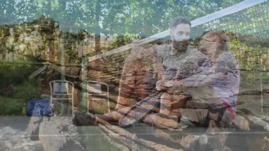 Tenis raketi tutan, arka planda ağaçlar olan taş duvarda oturan bir çift. Açık hava, boş zaman, spor, eğlence, aktivite, yaşam tarzı