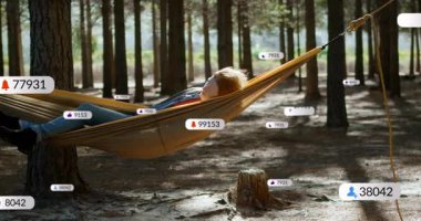 Ağaçlar arasındaki hamakta dinlenen, sosyal medya bildirimlerini izleyen kişi. Rahatlama, yalnızlık, dijital, boş zaman, doğa, kaçış