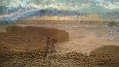 Dalgalar kumsala vuruyor, insanlar sahil boyunca ayak izleriyle yürüyor. Okyanus, sahil, deniz kenarı, doğa.