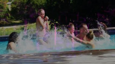 Yüzme havuzunda insanlar su sıçratır ve güneşli bir günde eğlenirler. Tatil, tatil, yaz, eğlence, su, aile.