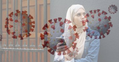 Akıllı telefonu tutan, dışarıda Coronavirus grafikleriyle gezen Müslüman bir kadın. Teknoloji, iletişim, sağlık, salgın hastalık önleme, sağlık hizmetleri