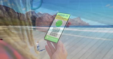 Elinde QR kodlu bir akıllı telefon olan bir kadın plajda yürüyen beyaz bir kadına karşı. covid-19 aşı sertifikası ve sağlık kartı konsepti