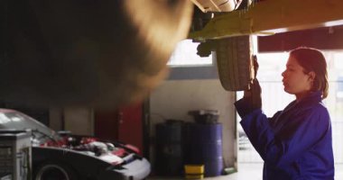 Araç kaldırmada lastik kontrolü, garajda çalışan mavi üniformalı bir tamirci. Otomotiv, bakım, onarım, atölye, teknisyen, servis