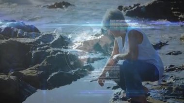 Okyanus kıyısındaki kayalarda oturan yaşlı insan dijital ağın animasyonunu izliyor. Teknoloji, doğa, bağlantı, son sınıf, sanal gerçeklik, açık hava