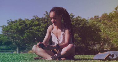 Çimlerin üzerinde oturan akıllı telefon kullanan Afrikalı Amerikalı kadınlara karşı bir ışık lekesi. küresel ağ ve teknoloji kavramı