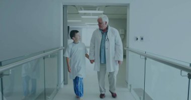 Doktor steteskop takıyor ve hastasıyla düz koridorda cam parmaklıklar ve sağlıkla yürüyor. Bakıcı, pediatri, klinikler, şefkat, güven, sağlık, sağlık