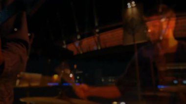 Müzik sahnesinde mikrofona yaslanmış sakallı bir vokalist. Yüzük ışığı, hareketli neon-mavi aksanlar. Performans, müzik, gece hayatı, sahne, ışıklandırma, mikrofon, eğlendirici