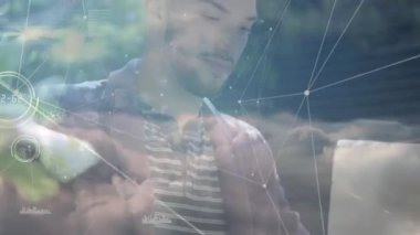 Adam açık havada teknolojik verilerle etkileşimde, yüzen ağ çizgileri, grafikler ve bulut görselleri gösteriyor. Teknoloji, veri, görselleştirme, bağlantı, yenilik, açık hava, doğa