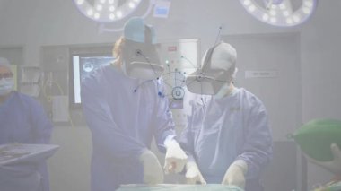 Tıbbi tiyatroda ameliyat yapan iki cerrah, VR kulaklık takıyor ve animasyon monitörlü far takıyor. Tıbbi, yenilik, teknoloji, klinik, yüksek teknoloji, hassasiyet, takım çalışması