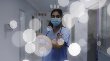 Kadın hemşire, tıbbi koridorda kolları çapraz duruyor, yüzen bokeh kaplamaları ve ikonlar var. Sağlık, tıbbi, profesyonel, klinik, esneklik, hijyen, çevre