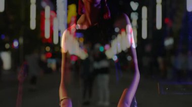 İş caddesinde püsküllü küpe takan bir kadın yanında neon çizelge yüzüyor. Modern, gece hayatı, canlı, şehir manzarası, moda, cazibe, eğlence