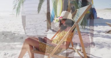 Sahildeki iskemlede dizüstü bilgisayarda yazan bir kadın, yüzen teknik çizelgeler ve güneş ışığında sörf tahtaları gösteriyor. Tropik, rahatlatıcı, açık hava, boş zaman, yaz, yaşam tarzı, canlı