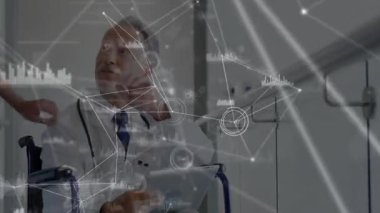 Klinikte tablet kullanarak tekerlekli sandalyede oturan kıdemli erkek doktor, animasyon ağı grafikleri sergiliyor. Tıbbi, sağlık, klinik, teknoloji, yenilik, profesyonel, iletişim