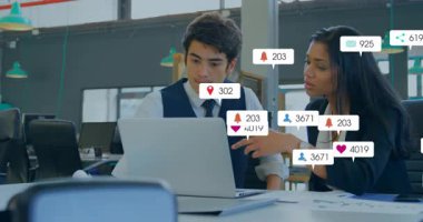 Ofiste dizüstü bilgisayarı inceleyen iki pazarlama meslektaşı yüzen sosyal medya nişan ikonları gösteriyor. İşbirlikçi, takım çalışması, modern, dijital, ağ oluşturma, profesyonel, çalışma alanı