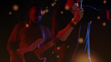 Şarkıcı mikrofon tutuyor ve gitar çalıyor. Müzik sahnesinde canlı parçacıklarla gitar çalıyor. Göstericiler, neon ışıklar, canlı müzik, enerjik, atmosferik, performans, gece hayatı