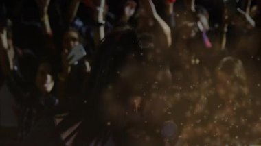 Sahnenin solundaki mikrofon sahnesinde şarkı söyleyen kadın şarkıcı, seyirci telefonlarına müzik ikonları yerleştiriyor. Performans, eğlence, coşku, konser, gece hayatı, sahne, kutlama
