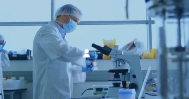 Erkek bilimadamı biyomedikal laboratuvarda örnek şişesi pipetliyor ve animasyon veri tabloları havada asılı duruyor. Bilim insanları, araştırma, yenilik, bilim, laboratuvar, deney, işbirliği