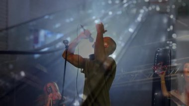 Kadın mikrofona şarkı söylüyor, yürüyen merdivenleri örtüyor, adam el kol hareketi yapıyor ve bavulu yuvarlıyor. Kentsel, seyahat, eğlence, performans, hareket, modern, canlı