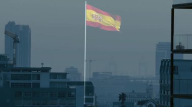 İspanyol bayrağı, sisli şehir siluetinin üzerinde sallanıyor. Vinçler görünüyor, palmiye ağaçları düz dizayn edilmiş. Vatansever, siluet, mimari, kentsel, sivil, hükümet, amblem