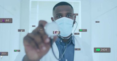 Maskeli doktor, dijital sağlıkta kameraya steteskop tutuyor ve sosyal medya simgeleri gösteriyor. Tıbbi uzman, teletıp, sağlık hizmeti, dijital iletişim, klinik ortam, profesyonel, sağlık teknolojisi