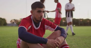 Futbol oyuncusu çimlerin üzerinde oturuyor, kalp ikonu ve grafiğini gösteriyor, sağlığa uygunluğu ölçüyor. Atletizm, takım çalışması, dayanıklılık, canlılık, açık hava, spor giyimi, kararlılık